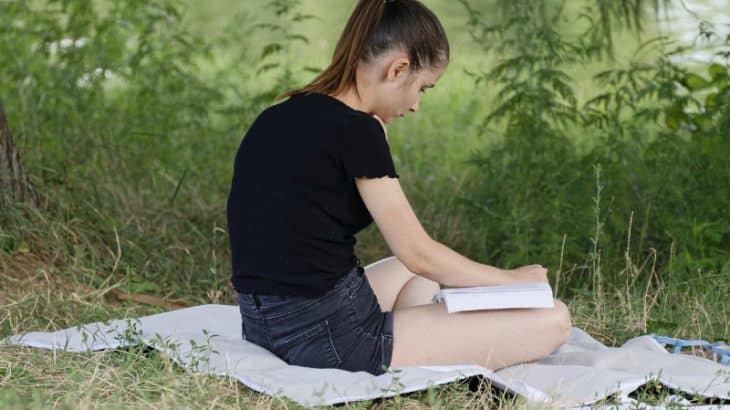 a girl reading a book on a blanket in the grass