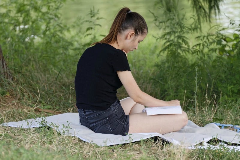 a girl reading a book on a blanket in the grass