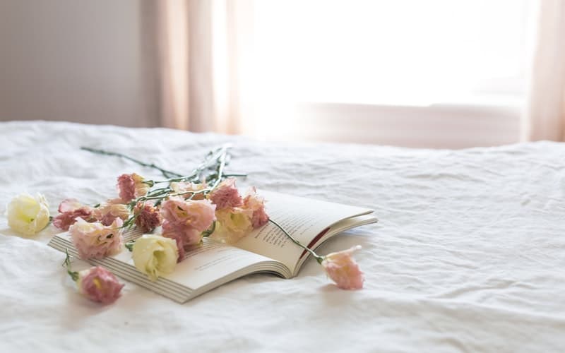 a book and flowers on a white bedspread