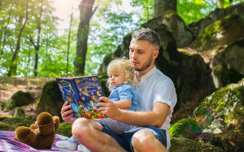 a father reading to a child beneath a tree