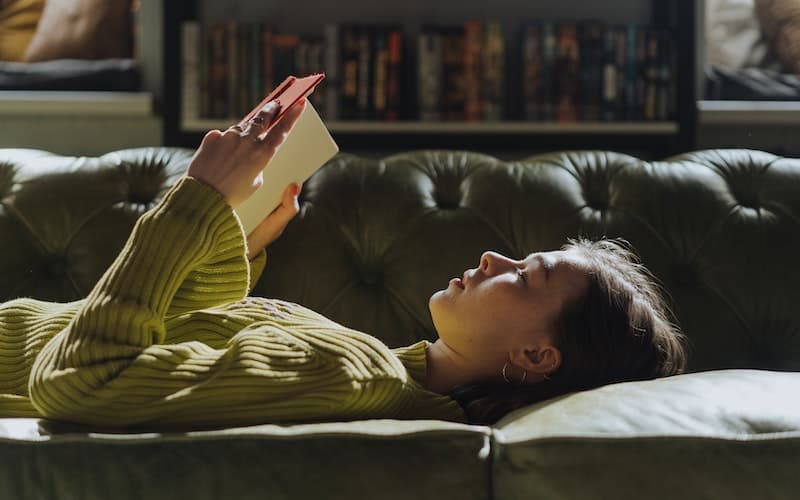 a teen reading a book while laying on the couch