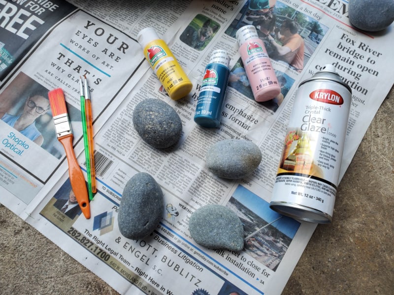 supplies to paint rocks on newspaper on the ground
