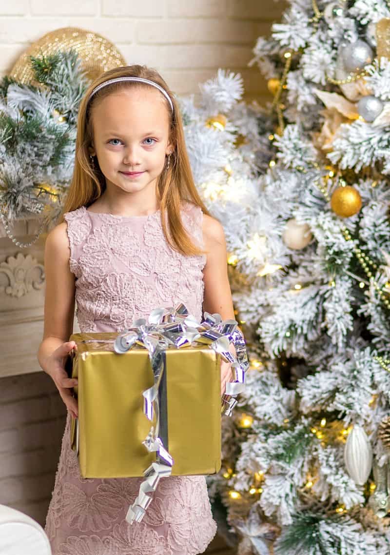 a child holding a present in front of a Christmas tree