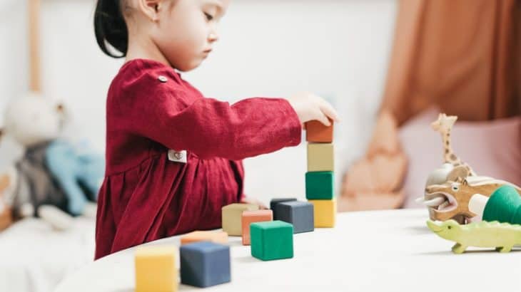 a girl in a red dress playing with wooden blocks