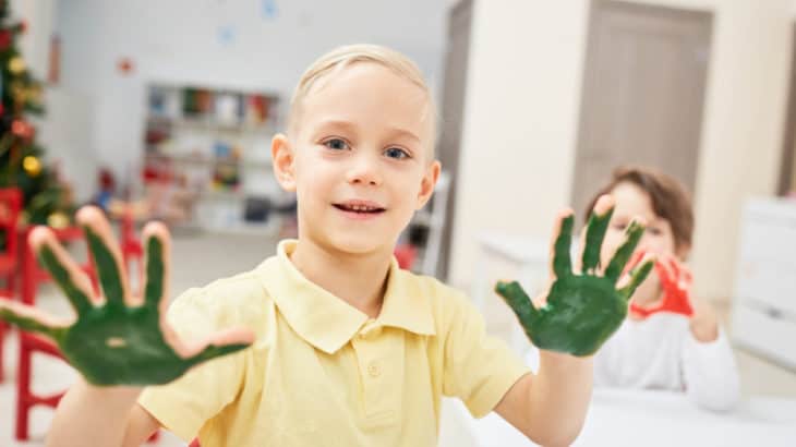 a boy holding up hands covered with green paint