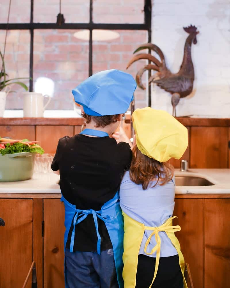 a boy and girl wearing aprons in the kitchen