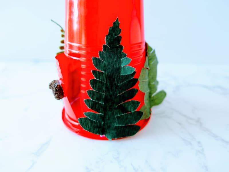 a red plastic cup with greenery glued on the sides