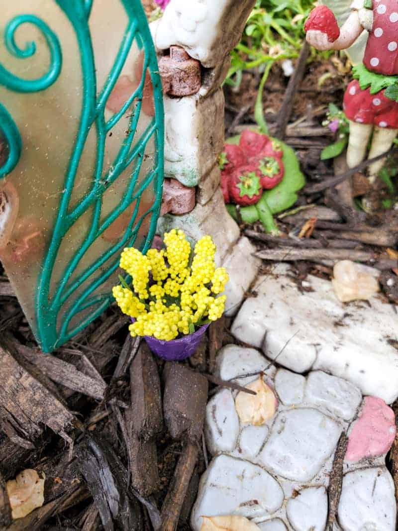 a miniature fairy garden pot with yellow flowers