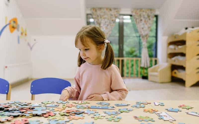 a little girl sitting at a table with a puzzle