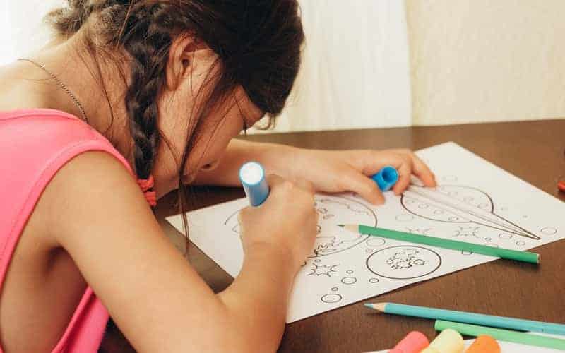 a girl coloring on a paper with markers and pencils