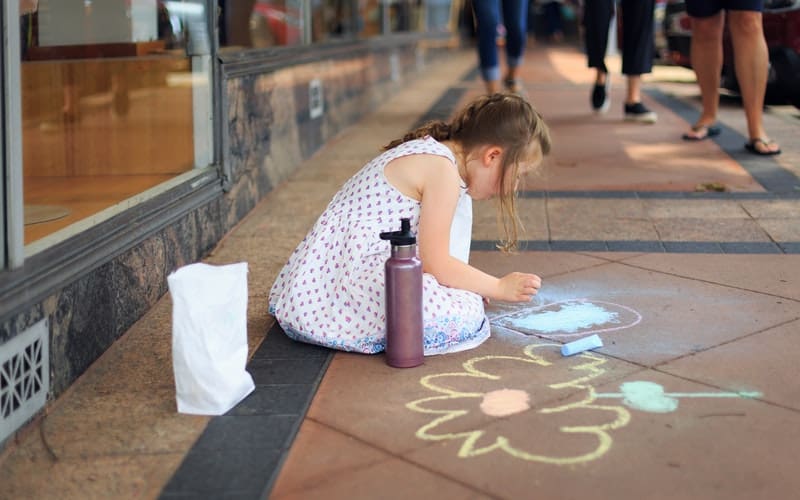 a girl drawing on the sidewalk in town
