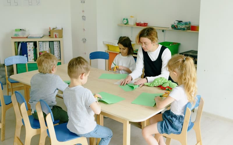 children sitting at a table cutting out green construction paper