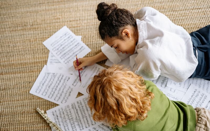 two girls laying on the floor looking at sheet music