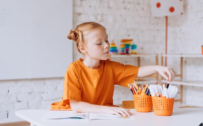 a girl sitting at a white table with markers coloring