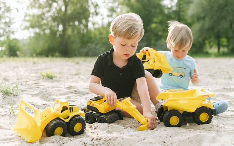 two boys playing in the sand with trucks