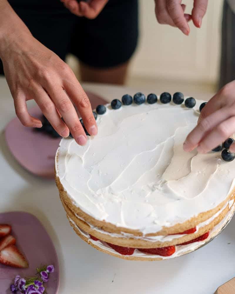 woman putting blueberries on a layer cake