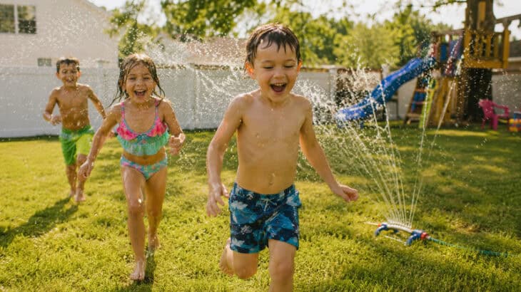 children running through the sprinkler in the backyard