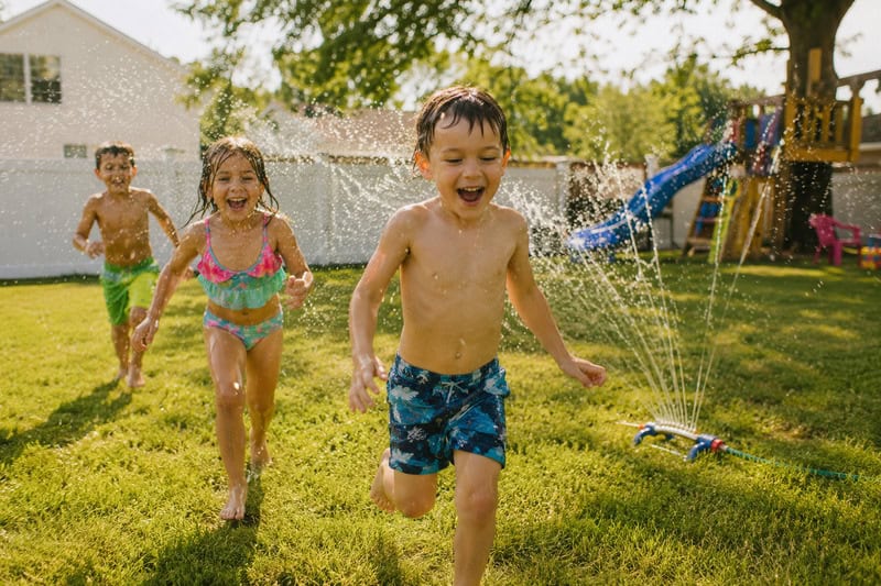 children running through the sprinkler in the backyard
